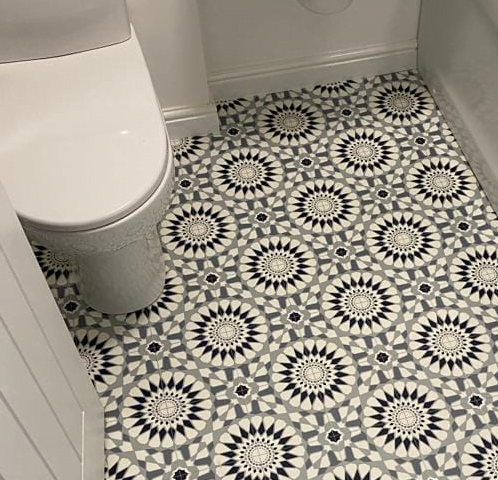 A bathroom featuring sleek vinyl flooring with a black and white geometric patterned tile, complemented by a pristine white toilet.