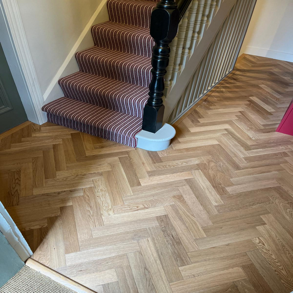 Staircase with striped carpet next to a herringbone-patterned wooden floor in a hallway.