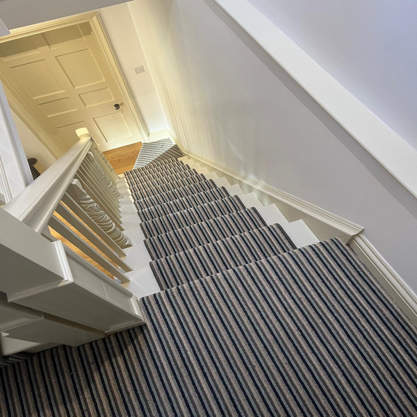 View of a carpeted staircase with striped pattern, leading down to a closed wooden door at the bottom.