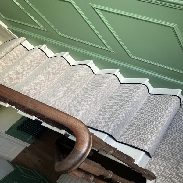 Staircase with a zigzag pattern carpet and a wooden handrail against a green paneled wall.